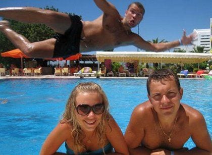 photo of a man diving behind a couple by the pool