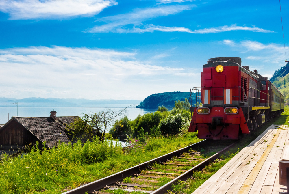 Summer landscape with the arrival of a red train on a wooden empty platform Trans-Siberian railway in village on shore Lake Baika